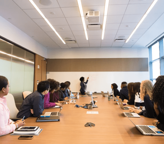 Pessoas em uma mesa longa prestam atenção em uma explicação